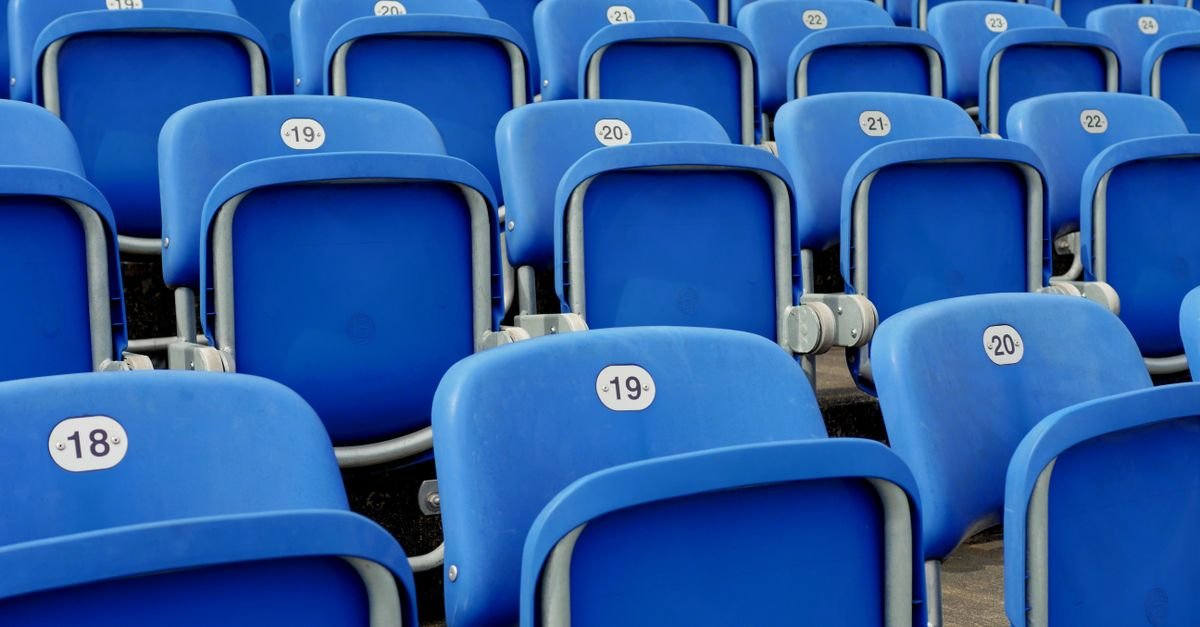 Fileiras de cadeiras azuis numeradas em arquibancada vazia de estádio