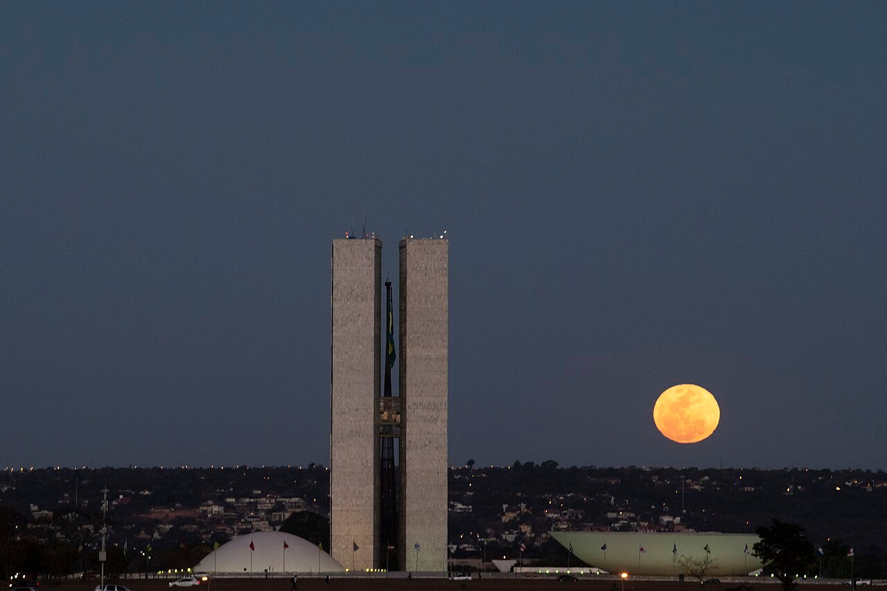 Fachada do Congresso Nacional, em Brasília, ao anoitecer, com a lua cheia ao lado das torres