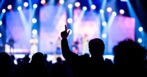 Plateia em silhueta com braços erguidos diante de palco iluminado em show