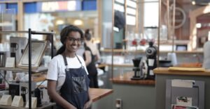 Empreendedora de avental sorri no balcão de uma cafeteria