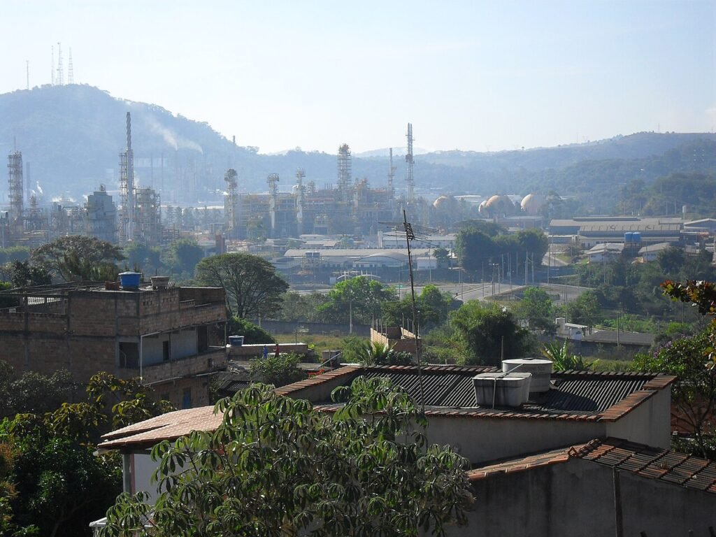 Vista de refinaria da Petrobras com torres e tanques industriais ao fundo de área residencial em Ibirité, Minas Gerais