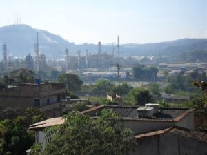 Vista de refinaria da Petrobras com torres e tanques industriais ao fundo de área residencial em Ibirité, Minas Gerais