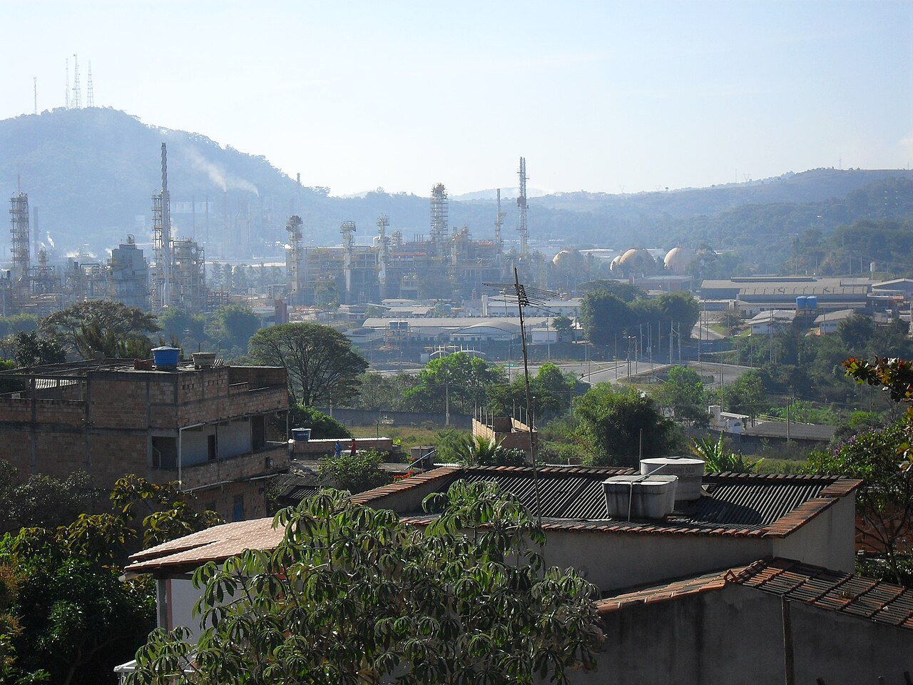 Vista de refinaria da Petrobras com torres e tanques industriais ao fundo de área residencial em Ibirité, Minas Gerais