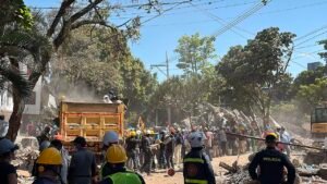 Equipes de resgate e moradores retiram escombros de um prédio desabado em Cali, na Colômbia, com policiais e caminhão no local
