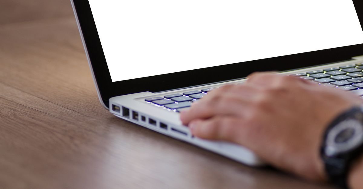 Mão sobre o teclado de um notebook com a tela em branco, sobre mesa de madeira