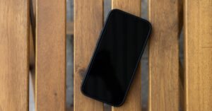 Celular preto com a tela apagada sobre uma mesa de ripas de madeira