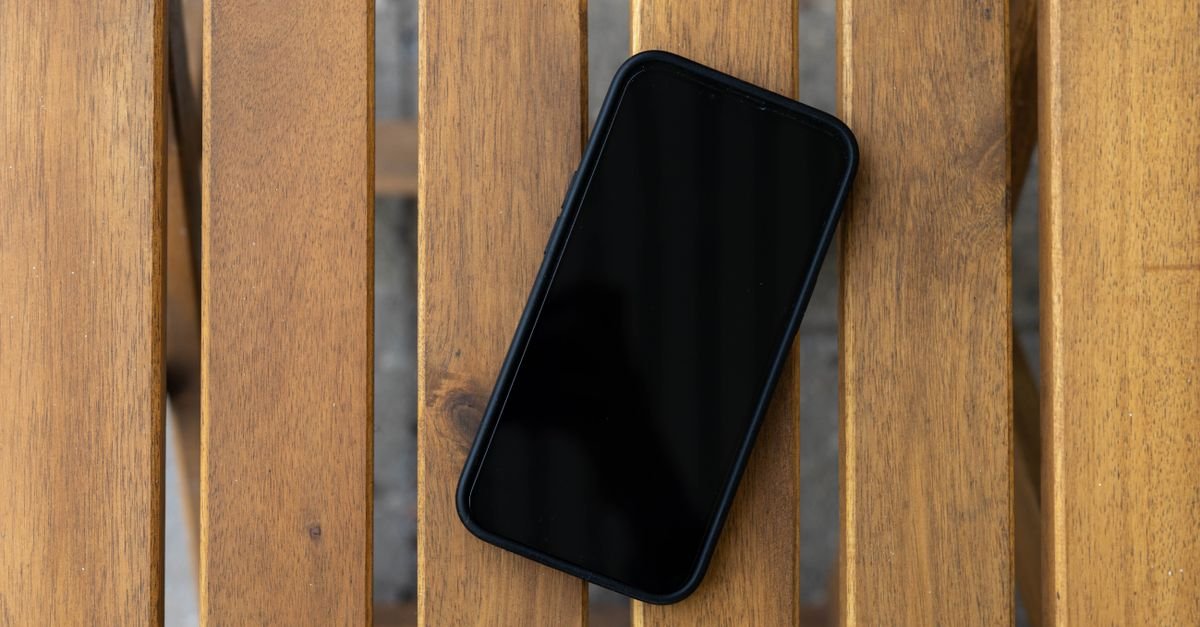 Celular preto com a tela apagada sobre uma mesa de ripas de madeira