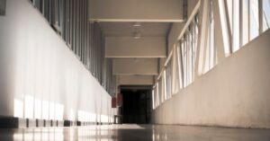 Corredor interno vazio de instituição de ensino, com luz natural entrando pelas janelas