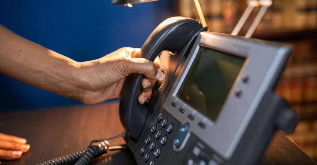 Mão retirando o fone de um telefone de mesa em atendimento
