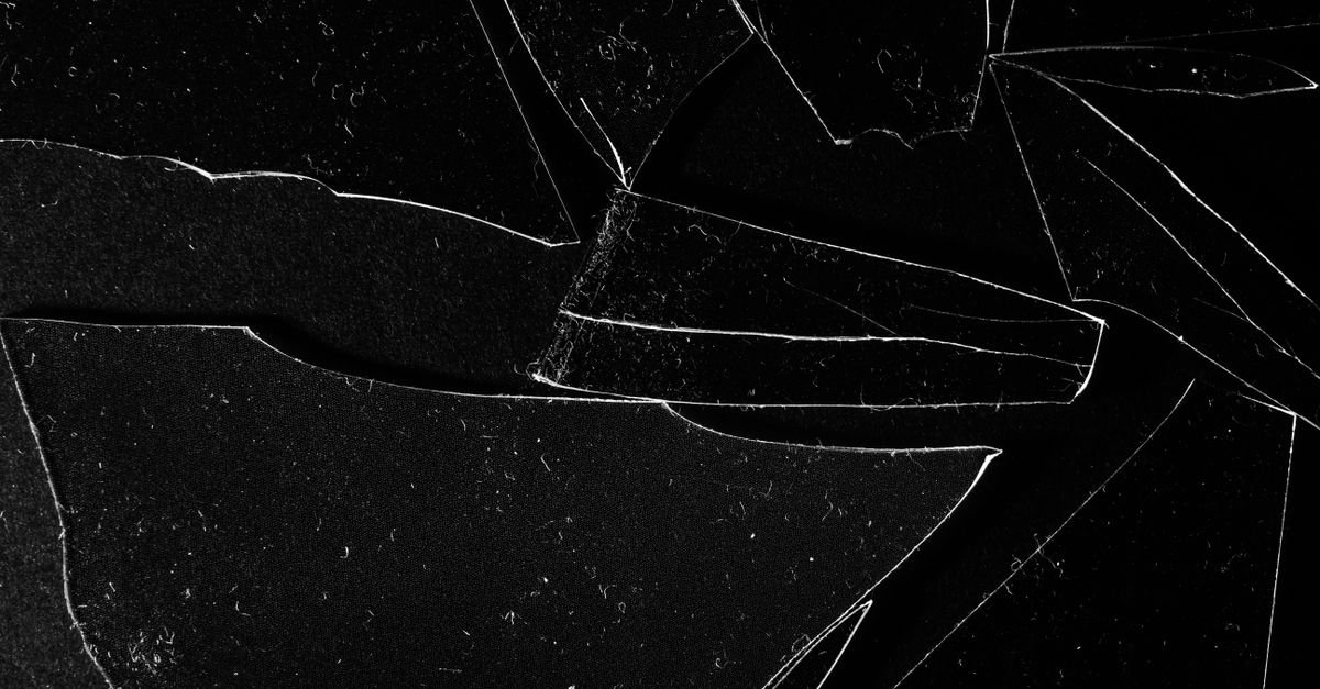 Close-up de vidro estilhaçado com trincas em fundo escuro