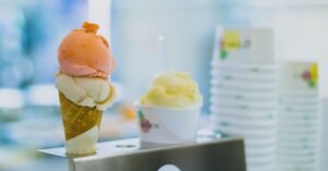 Casquinha de sorvete com duas bolas ao lado de pote de gelato em balcão de sorveteria