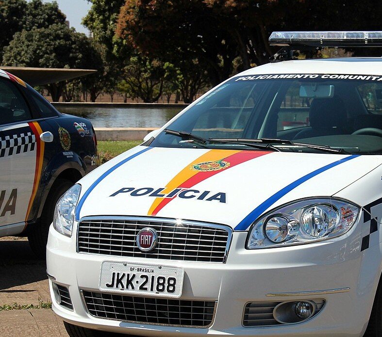 Frente de uma viatura branca da Polícia Militar do Distrito Federal com faixas coloridas e sinalizador no teto