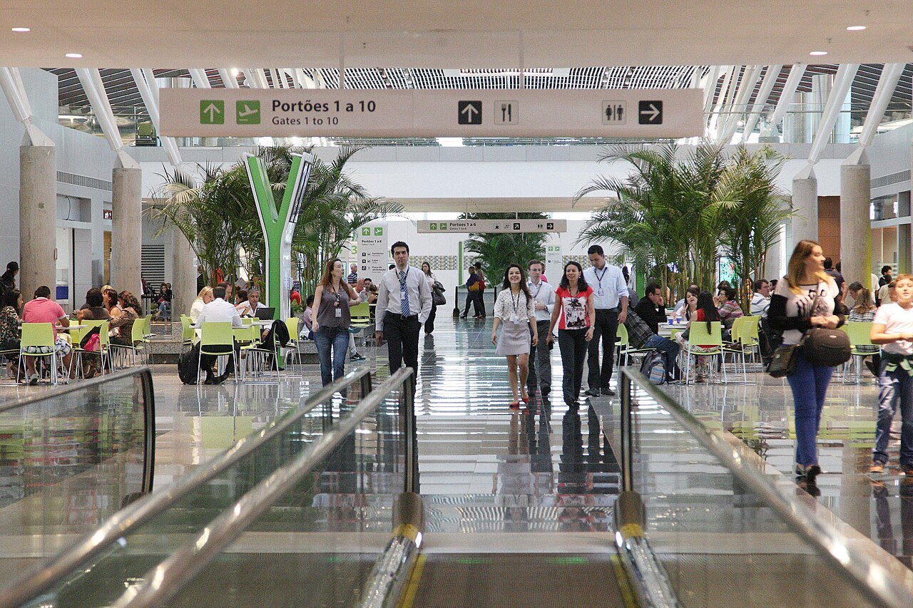 Saguão do Aeroporto Internacional de Brasília com passageiros e placa de portões de embarque