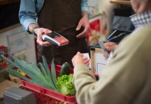 Atendimento no caixa de um mercado, com maquina de cartao e cesta de compras