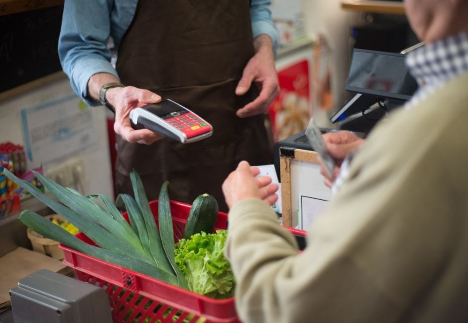 Atendimento no caixa de um mercado, com maquina de cartao e cesta de compras