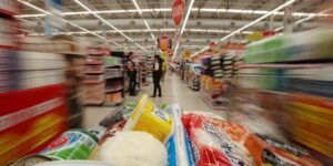 Consumidor empurra carrinho com alimentos em corredor de supermercado