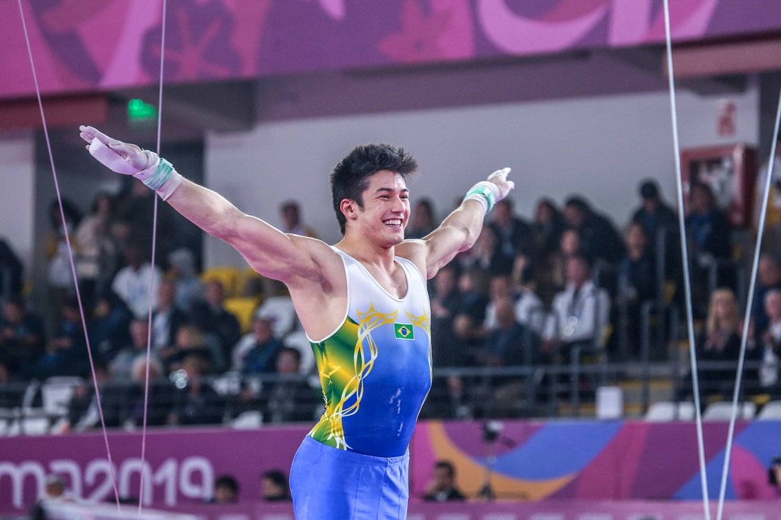 Ginasta Arthur Nory de collant verde e amarelo com os braços abertos após apresentação na barra fixa