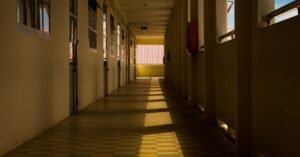 Corredor vazio de escola com luz do sol entrando pelas janelas e projetando sombras no piso