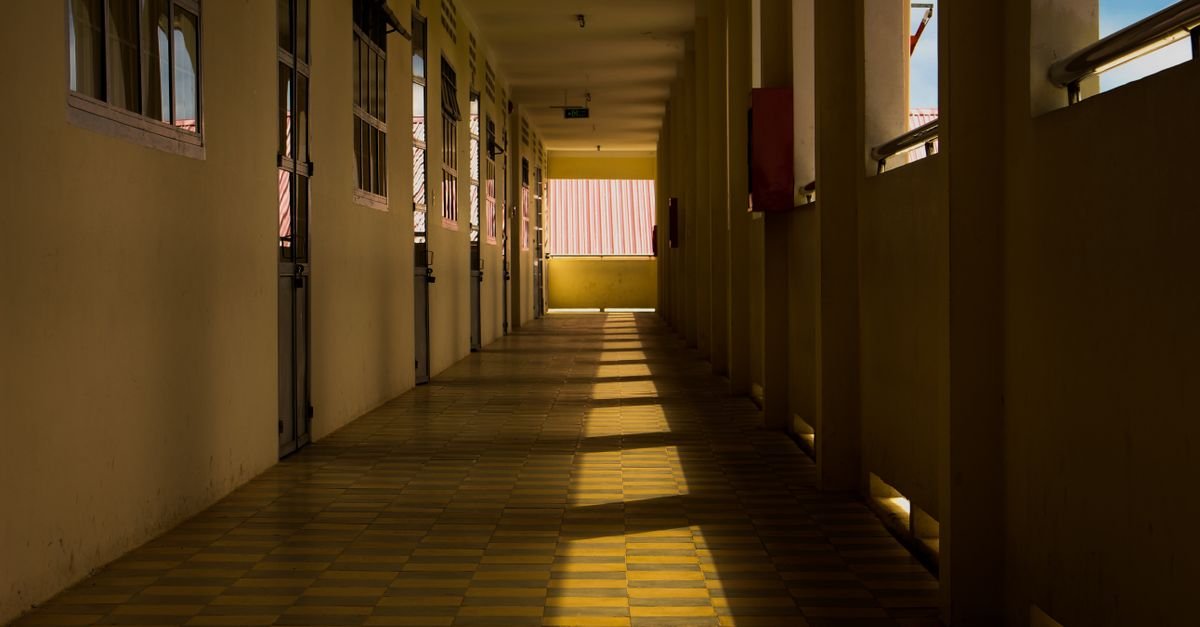 Corredor vazio de escola com luz do sol entrando pelas janelas e projetando sombras no piso