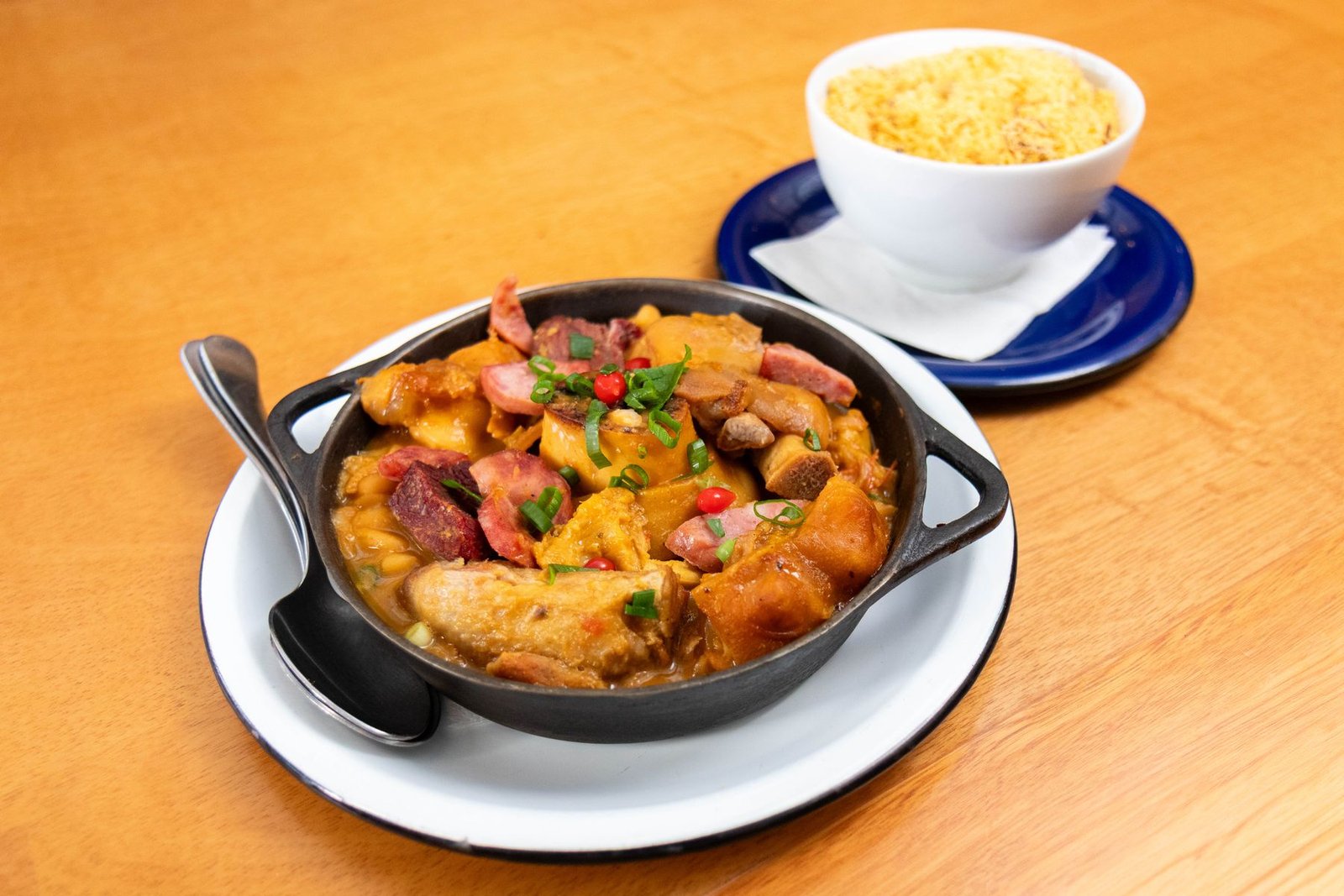 Panela de ferro com feijoada servida sobre prato branco, ao lado de tigela de farofa