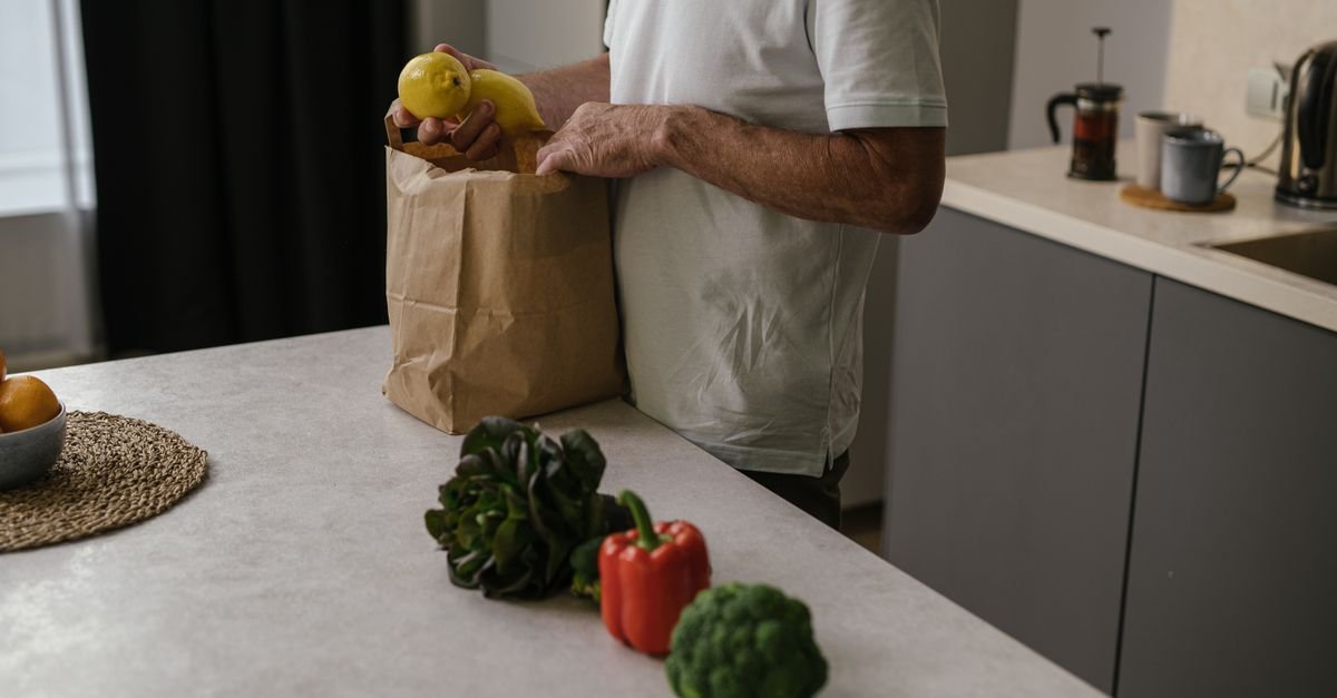 Pessoa retira frutas e legumes de uma sacola de papel sobre a bancada da cozinha