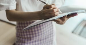 Mão de estudante escrevendo com caneta em um caderno aberto