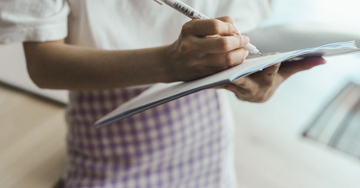 Mão de estudante escrevendo com caneta em um caderno aberto