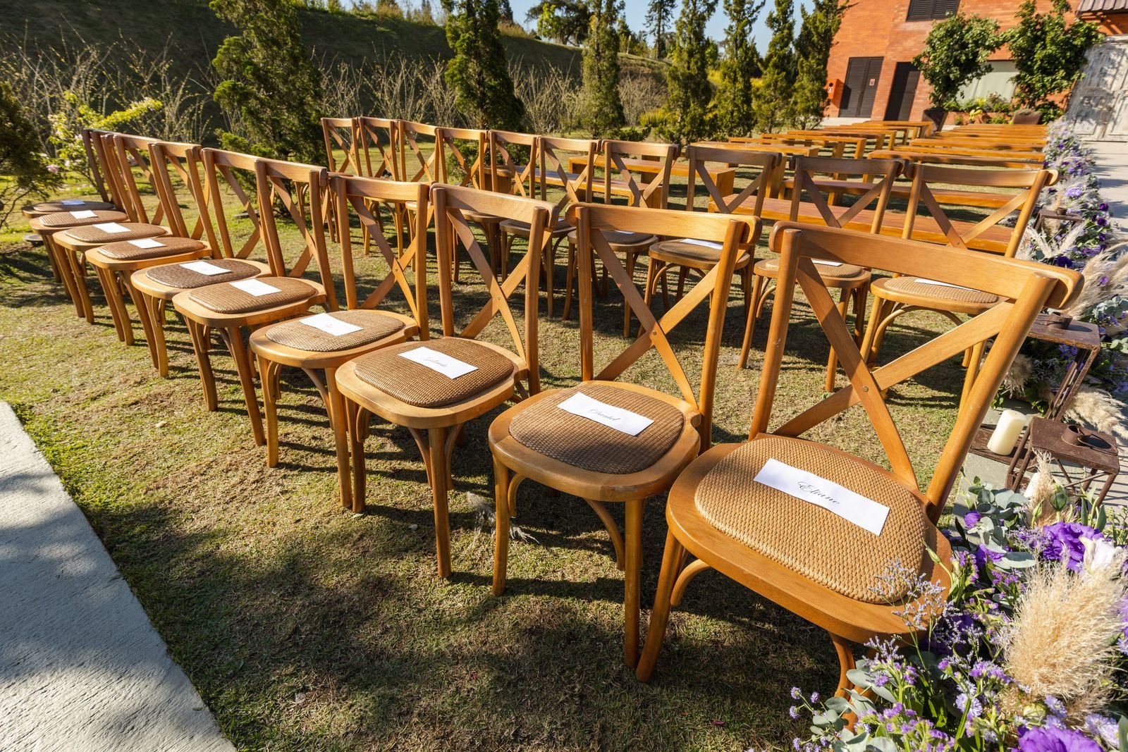 Cadeiras de madeira vazias, enfileiradas em gramado, montadas para uma cerimônia de casamento ao ar livre