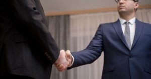 Dois executivos de terno apertam as mãos durante reunião de negócios