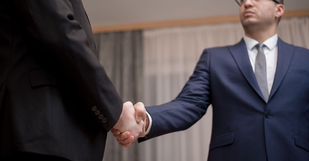 Dois executivos de terno apertam as mãos durante reunião de negócios