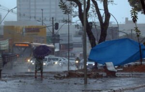 Pedestre com guarda-chuva atravessa via alagada durante chuva forte em Ceilândia