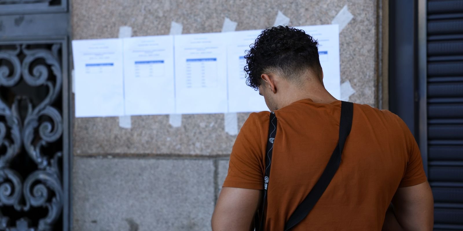 Candidato de costas consulta listas de resultado de concurso afixadas em parede