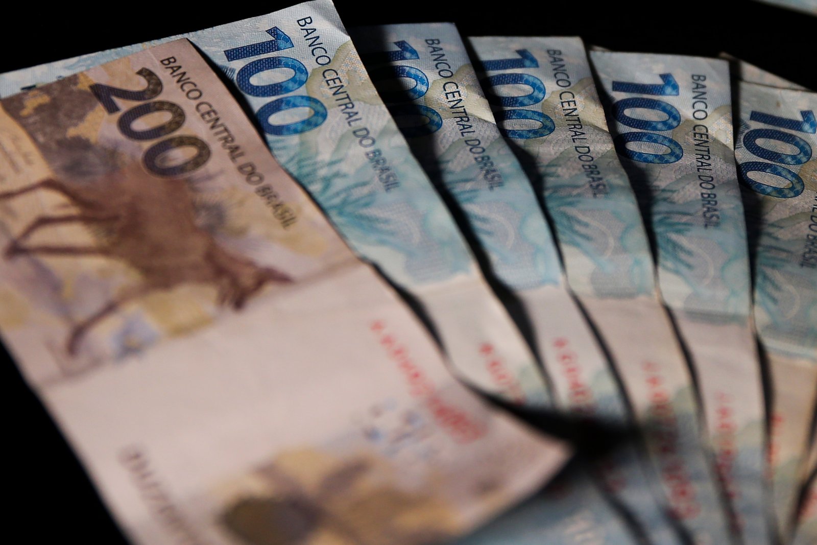 Cédulas de R$ 200 e de R$ 100 do real abertas em leque sobre fundo escuro