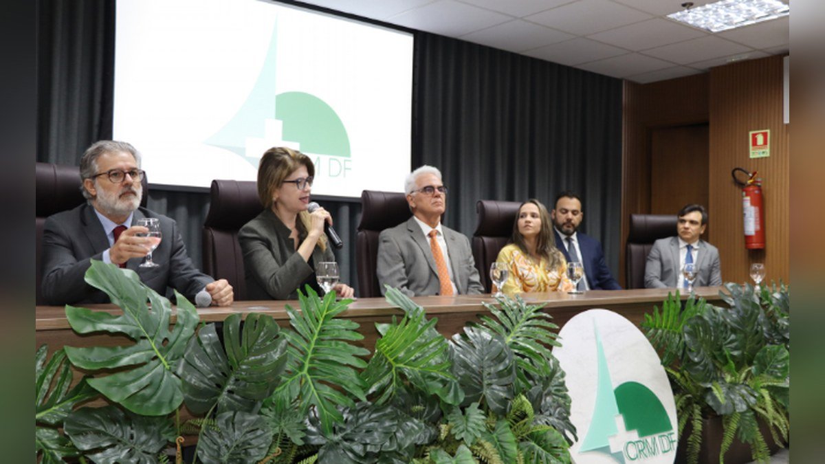 Mesa de autoridades durante o lançamento da campanha do Conselho Regional de Medicina do Distrito Federal, com o logotipo do CRM-DF ao fundo