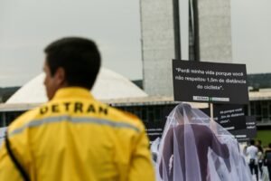 Agente do Detran-DF em ação educativa de trânsito com placas de conscientização em frente ao Congresso Nacional