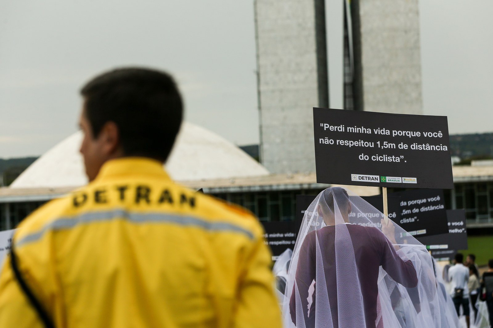 Agente do Detran-DF em ação educativa de trânsito com placas de conscientização em frente ao Congresso Nacional