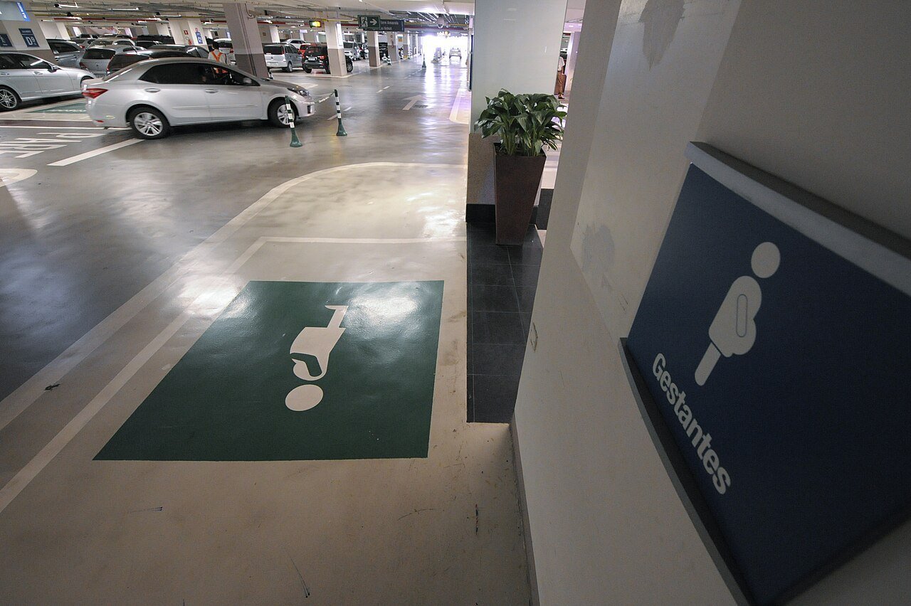 Vaga de estacionamento reservada a gestantes, com pintura verde no piso e placa azul indicando o uso
