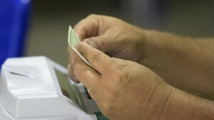 Mãos de eleitor junto a uma urna eletrônica da Justiça Eleitoral, com lacre verde