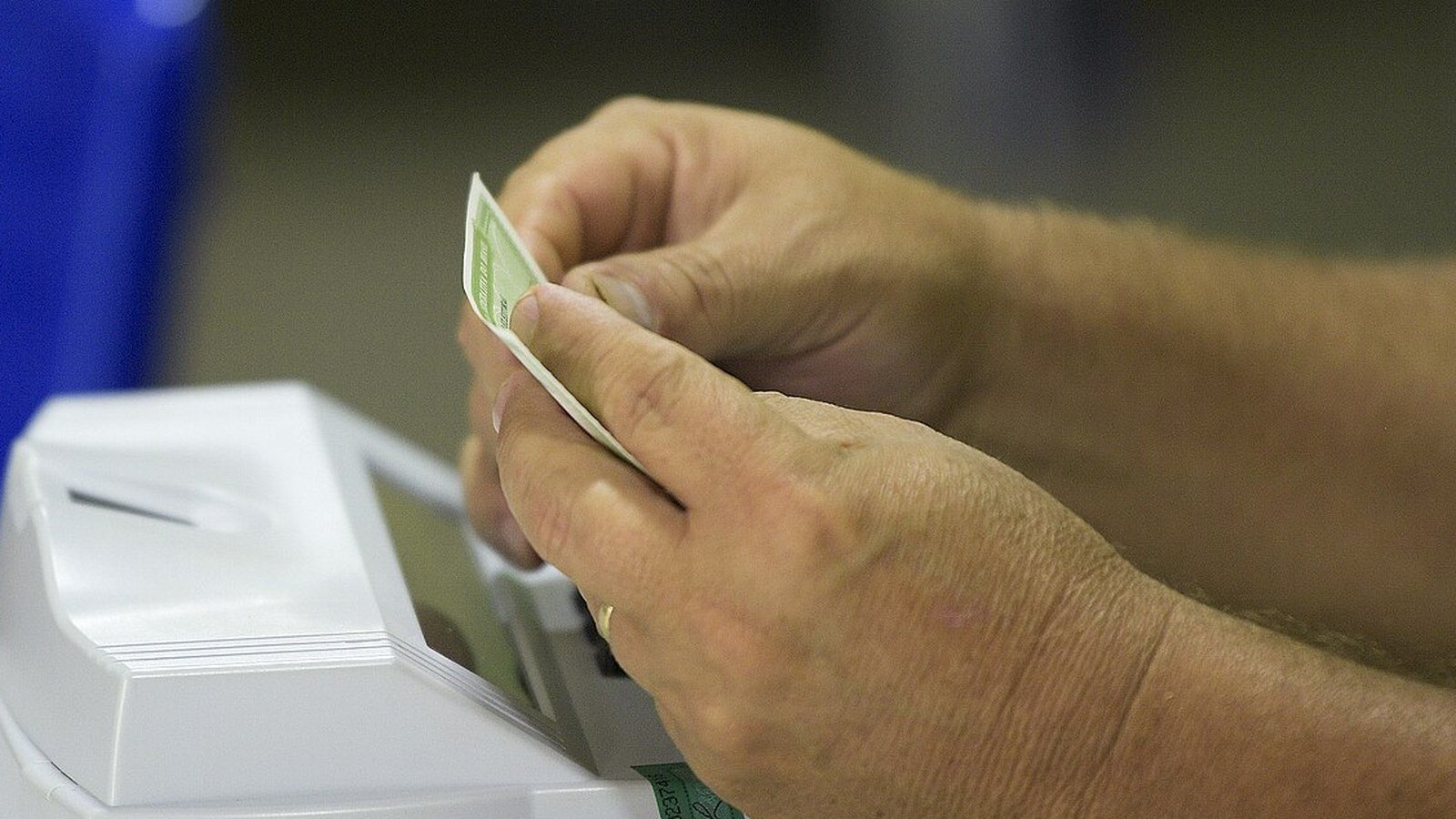 Mãos de eleitor junto a uma urna eletrônica da Justiça Eleitoral, com lacre verde
