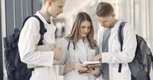 Três estudantes de medicina com jaleco branco conferem anotações em um corredor de universidade