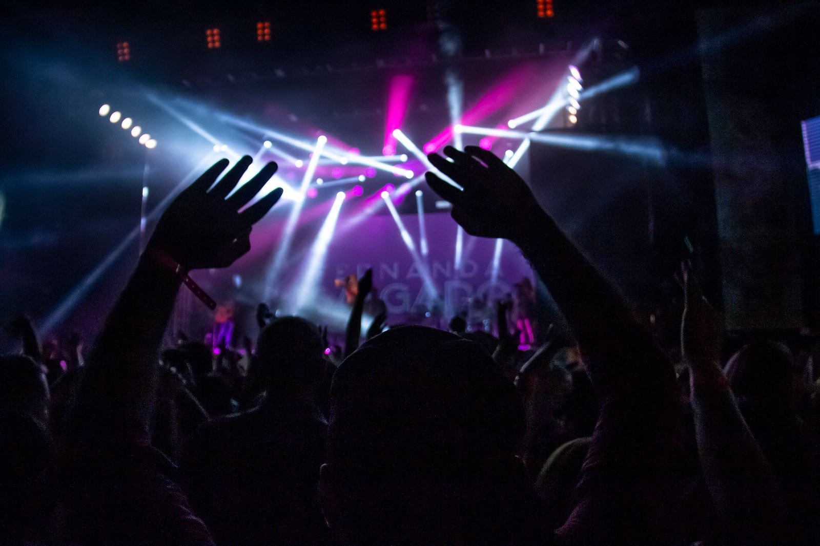 Público de braços erguidos diante de palco iluminado em show noturno