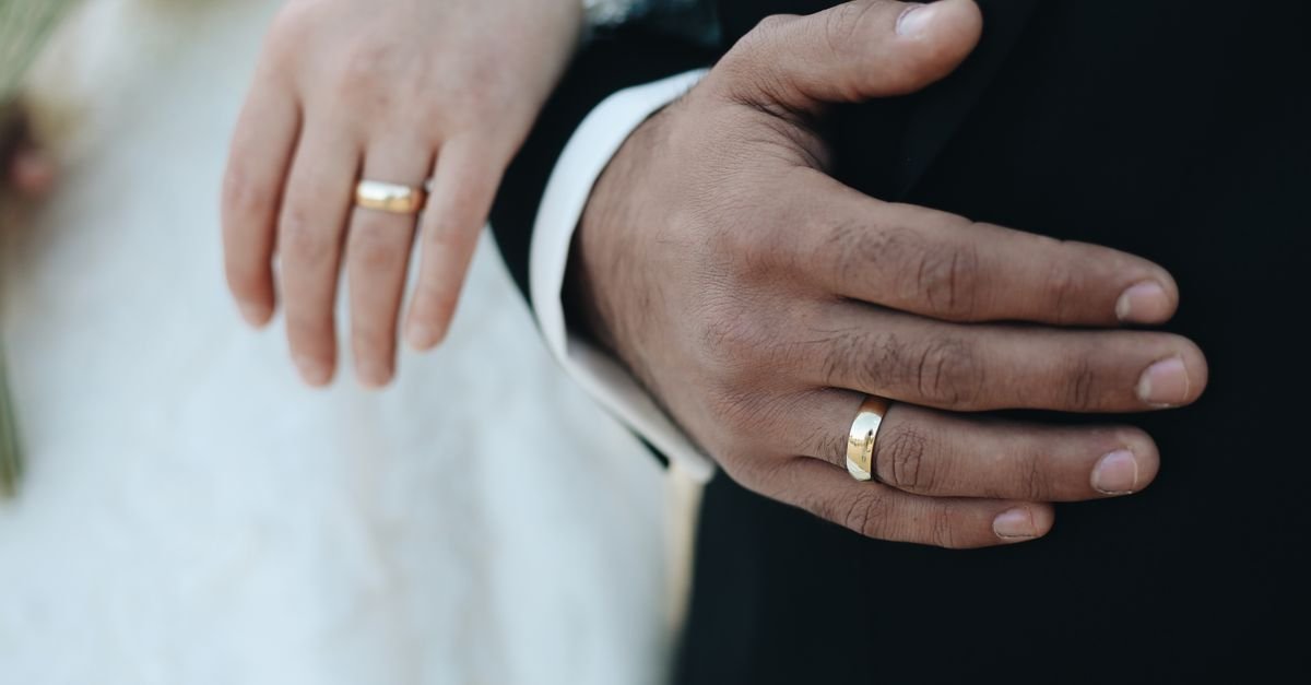 Mãos de casal com alianças douradas em cerimônia de casamento