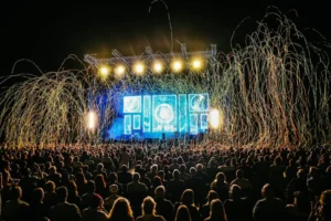 Público em festival ao ar livre diante de palco iluminado