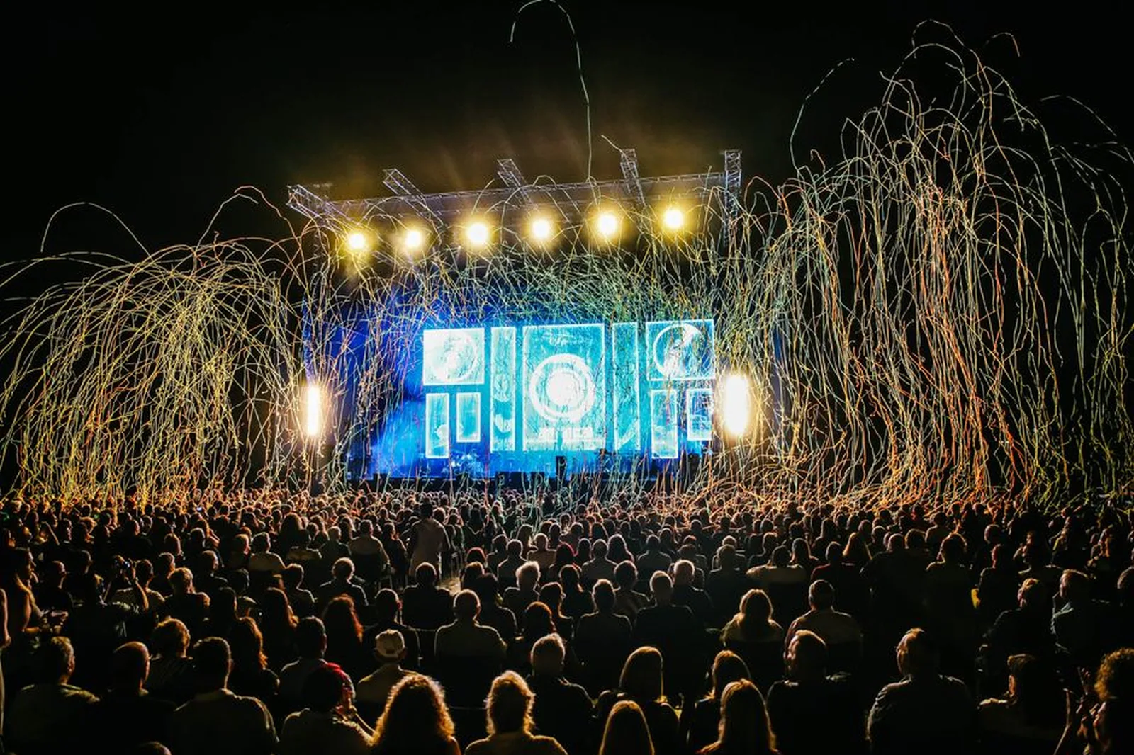 Público em festival ao ar livre diante de palco iluminado