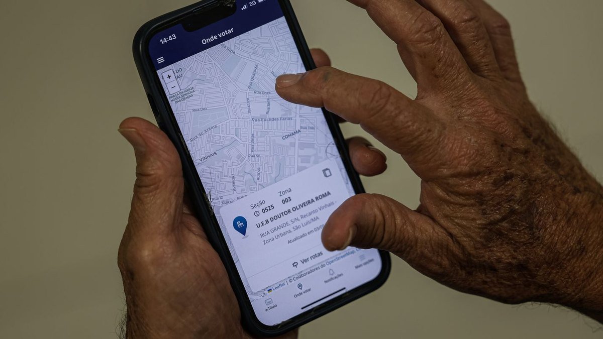 Mãos de eleitor seguram celular com a tela do aplicativo e-Título na função Onde votar