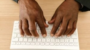 Mãos digitando em teclado de computador sobre mesa de madeira