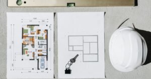 Planta baixa de projeto, capacete de obra branco, nível e chaves sobre superfície clara