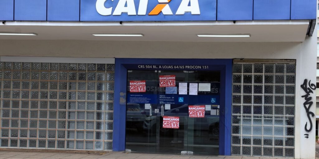 Fachada de agência da Caixa Econômica Federal com as portas fechadas e cartazes vermelhos de bancários em greve colados nos vidros