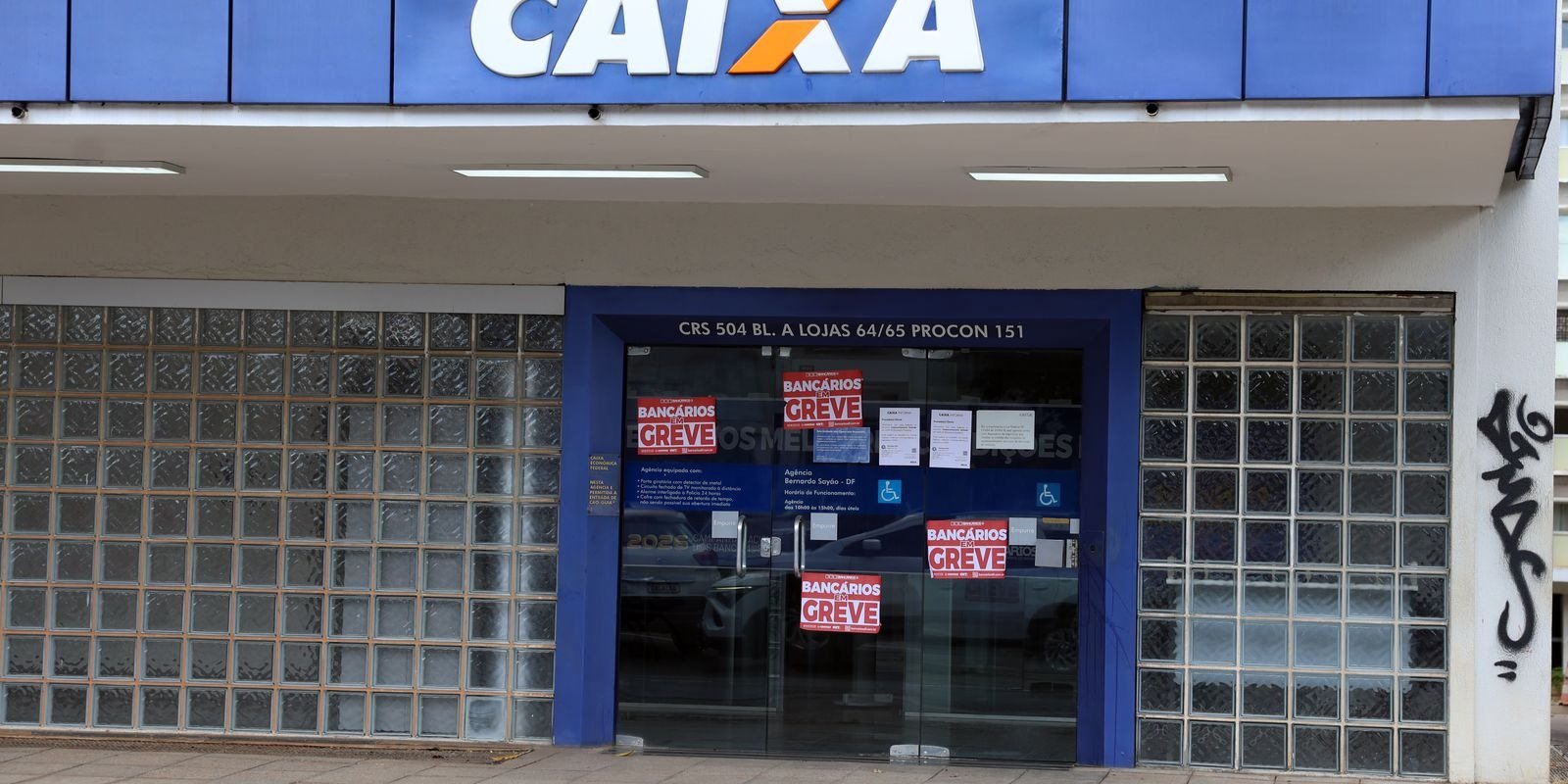 Fachada de agência da Caixa Econômica Federal com as portas fechadas e cartazes vermelhos de bancários em greve colados nos vidros