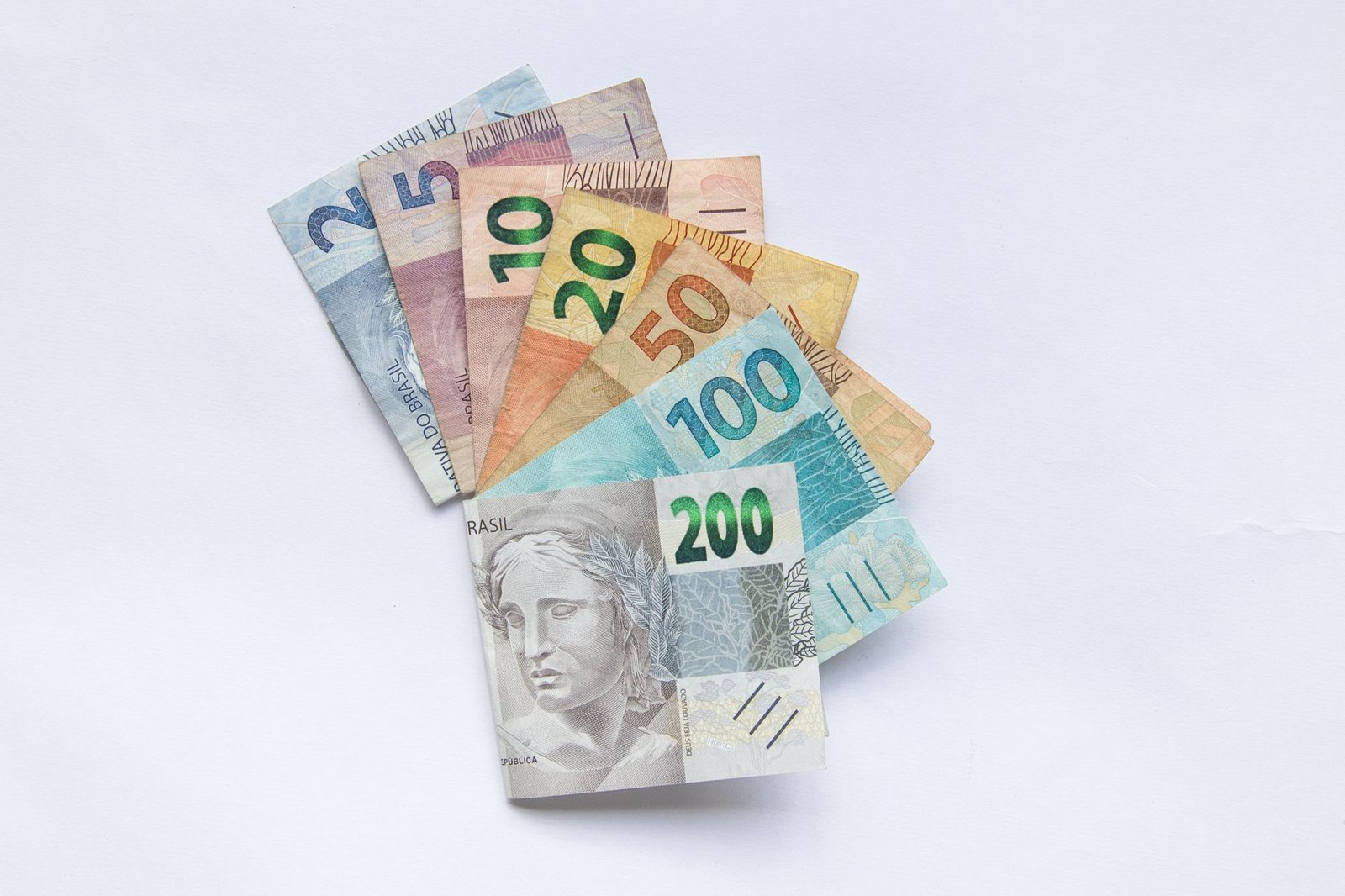 Cédulas de real brasileiras de 2, 5, 10, 20, 50, 100 e 200 abertas em leque sobre fundo branco